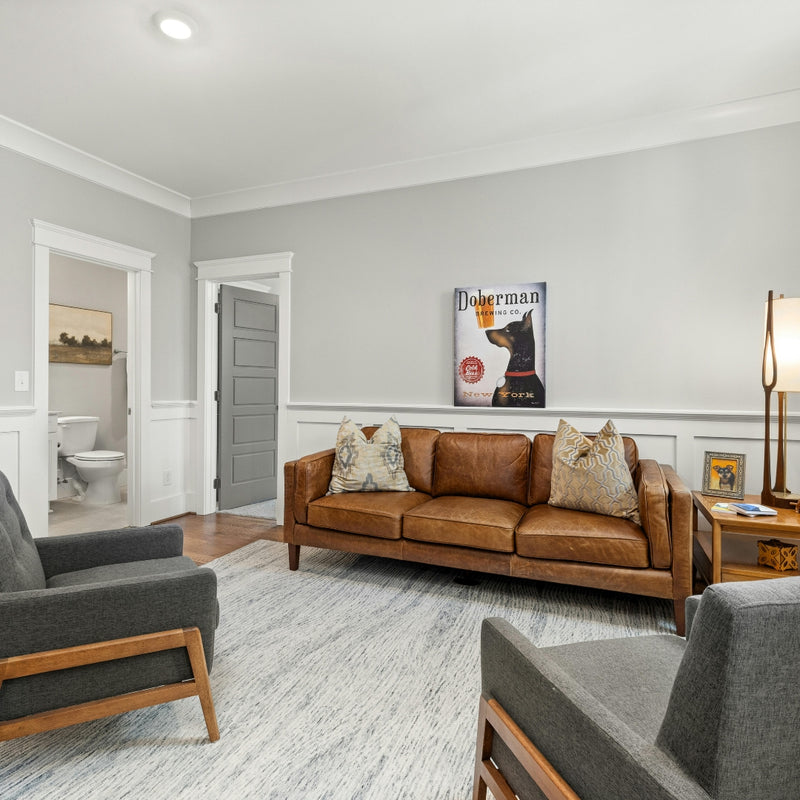 Living room with brown leather sofa, gray armchairs, and a dog-themed poster on the wall.