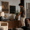 Man arranging decor items in a living room with textured wall art and furniture.