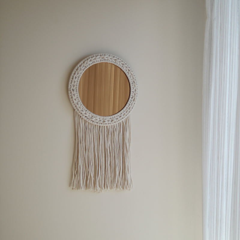 Round wooden mirror with macrame frame and fringe on a beige wall