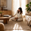 Woman arranging a pillow on a textured rug in a cozy living room.